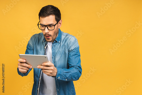 Leinwand Poster Amazed shocked happy bearded man using digital tablet looking shocked about social media news, astonished man shopper consumer surprised excited by online win isolated over yellow background