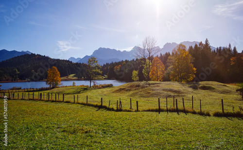 Herbststimmung in der Morgensonne im Voralpenland in den bayrischen Alpen mit Blick von einer Bergwiese auf den Geroldsee und Bergen im Hintergrund