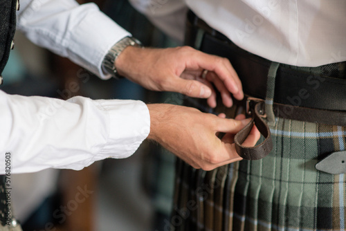 Mans hands fastening kilt belt on another man from behind close up