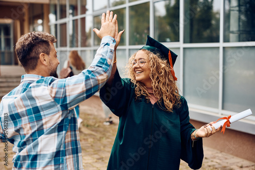Happy graduate student and her father giving high five after graduation ceremony. photo