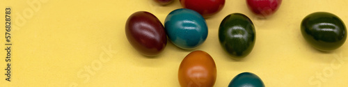 Banner 4x1. Colorful painted Easter eggs on a yellow textured background © Anna