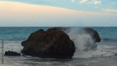 Slow motion video of waves crashing against a large boulder in the coastal zone photo