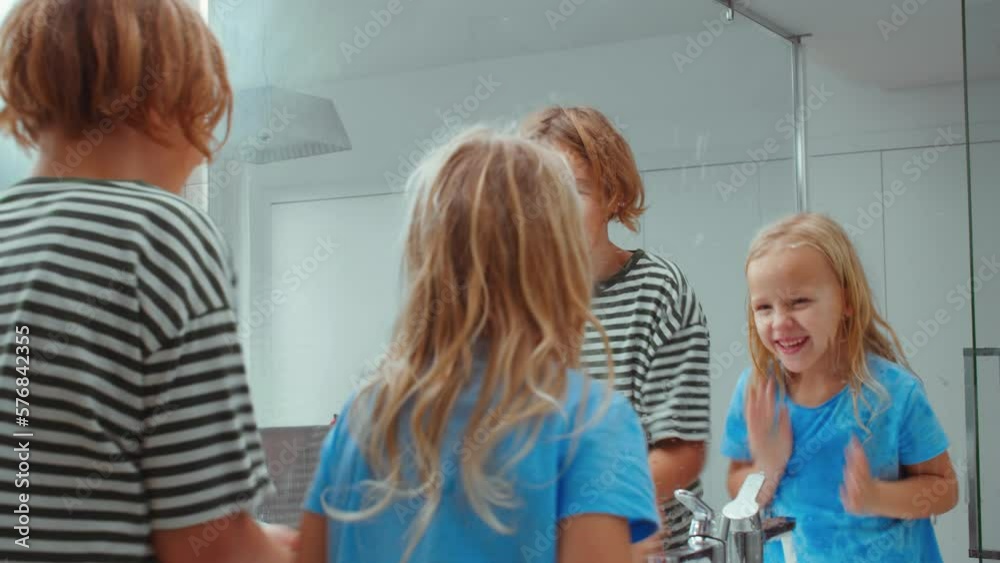Two siblings having fun splashing water and laughing while washing up together in the morning Two siblings having fun splashing water and laughing while washing up together in the morning