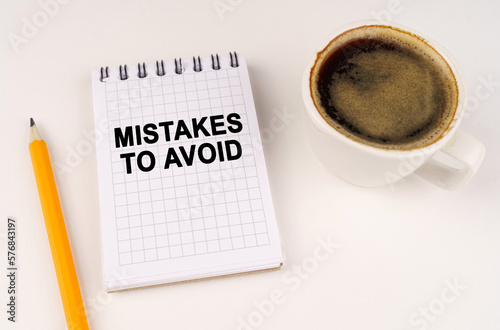 On a white surface, a cup of coffee, a pencil and a notepad with the inscription - Mistakes To Avoid