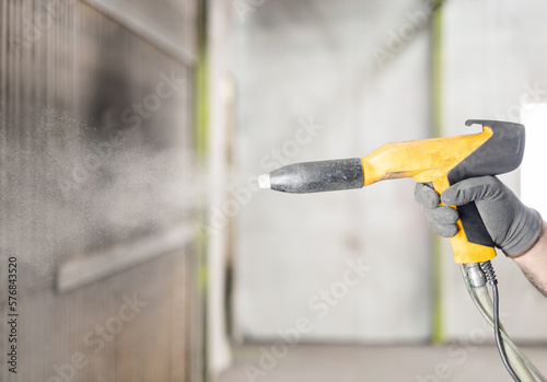 Detail of the hand of a man working in a factory finishing a job using the electrostatic powder coating technique with a spray gun. Metal factory works concept. photo