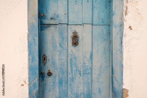 Old wooden door of colonial period house with peeling blue paint and rusty metal knocker and keyhole.