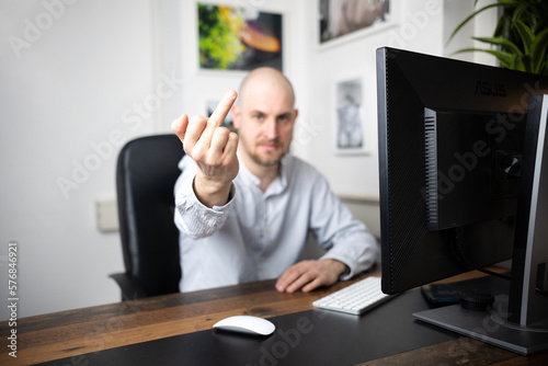 Angry employee shows middle finger in his office/home office after meeting for pitch and continues to make obscene gestures photo