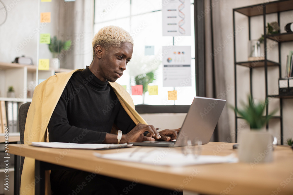 Successful african businessman in stylish suit working on laptop computer on modern office. Professional ceo managing environmental, social and corporate governance.