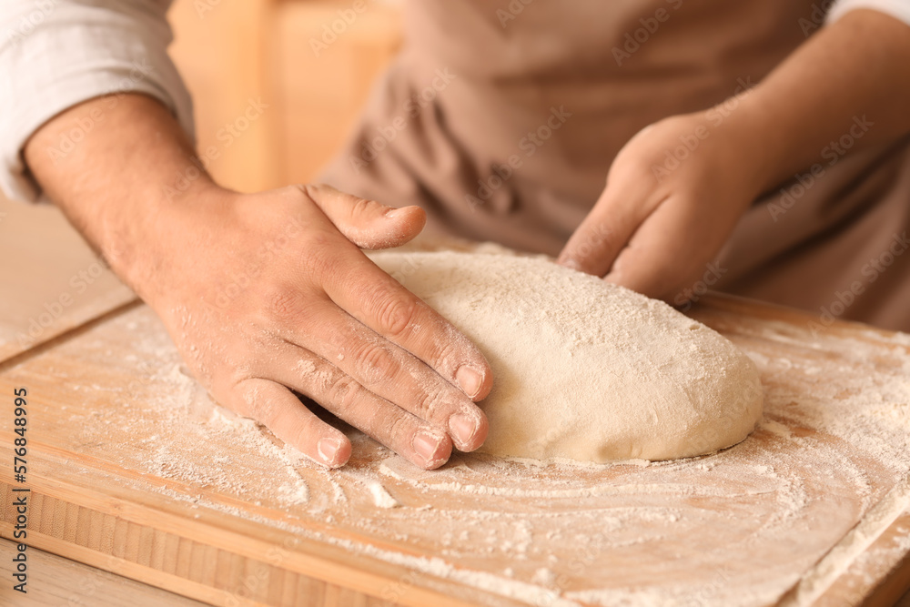 Male baker preparing dough for bread at table in kitchen, closeup