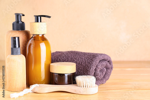 Set of cosmetic products, massage brush and towel on wooden table against color background
