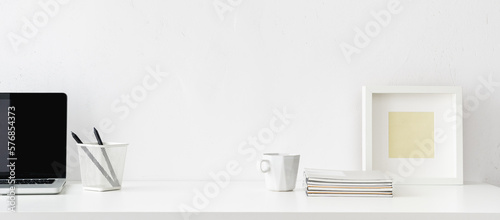 Desk with white office supplies, mug, frame, laptop and empty space. Mockup.