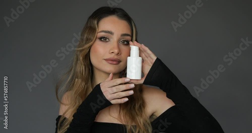 Charming young woman with professional makeup demonstrates white jar by blowing kiss to camera. Concept of beauty. 