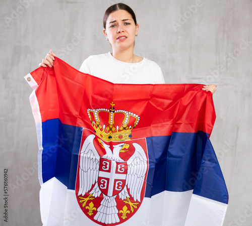 Frustrated girl with flag of Serbia in her hands. Isolated on gray background photo