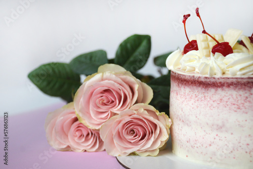 Pink Cake decorated with frosting and maraschino cherries. Half of the cake and fresh roses in the center  close up.