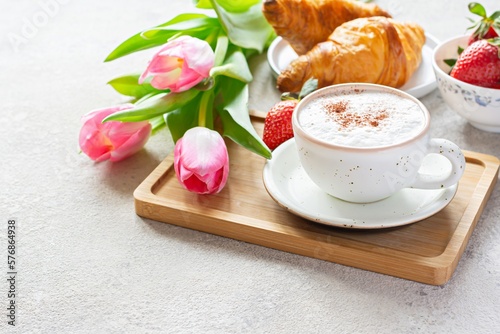 Happy mother's day, beautiful breakfast, lunch with cup of coffee (cappuccino) fresh croissants, strawberries on tray, bouquet of tulips as gift. Festive concept. Spring holiday, family relations.