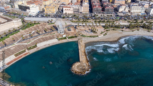 Fototapeta Naklejka Na Ścianę i Meble -  Panoramic view of the city of Civitavecchia with the adjoining tourist port and Forte Michelangelo. Emerald sea and view with tropical palm trees. Ferris wheel and cloudy sky.