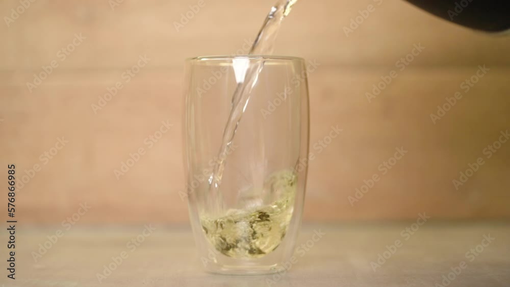 Boiling water flows from kettle into glass of tea leaves, then quickly then slowly, speed ramp. Boiling water flows from kettle into glass of tea leaves, then quickly then slowly, speed ramp.