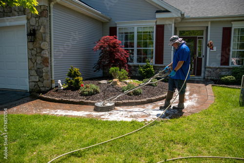 Handyman using a circular power washer to clean a brick walkway in front of a house