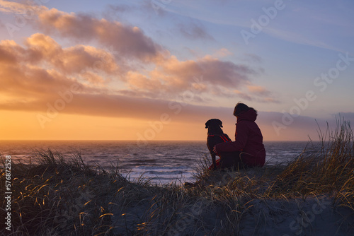 Fototapeta Naklejka Na Ścianę i Meble -  Women with her dog watching the sunset at the beach. High quality photo