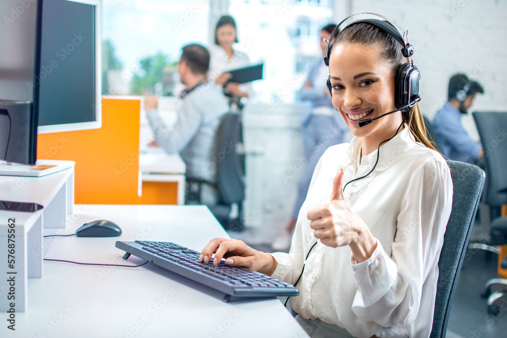 Portrait of smiling woman with headset showing approve sign with thumb up to camera at call center office. Portrait of smiling woman with headset showing approve sign with thumb up to camera at call center office.