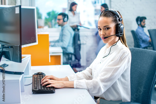 Foto Portrait of female IT sector operator with headset working on computer and looking at camera in call center office