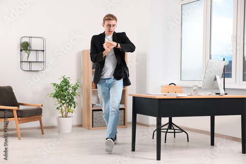 Emotional young man checking time while walking in office. Being late photo