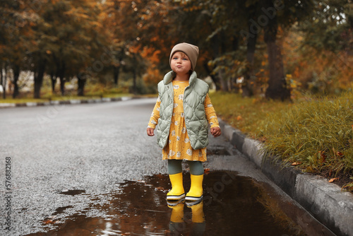 Cute little girl standing in puddle outdoors, space for text