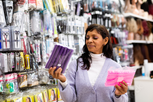 Portrait of smiling hispanic woman shopping in hair care cosmetics and accessories store, choosing new curlers.