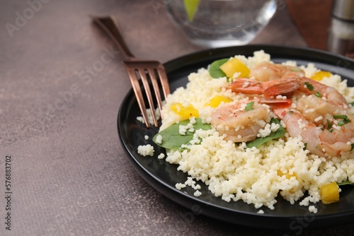 Tasty couscous with shrimps, bell pepper and basil on brown textured table, closeup. Space for text
