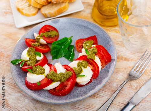 Caprese salad with tomatoes, mozzarella cheese, fresh basil and pesto on plate, Mediterranean food