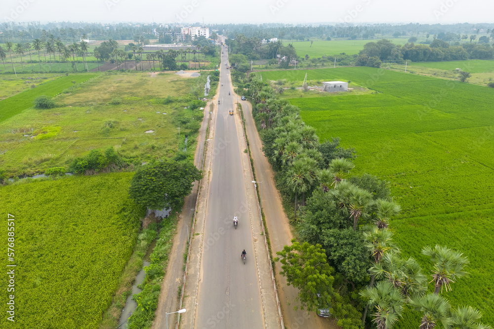 Aerial view of rural road passing through paddy fields in Guntur district, Andhra Pradesh state in India.