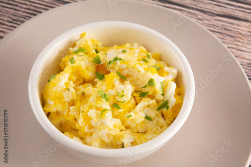 Scrambled eggs on bowl, wooden table, close up view
