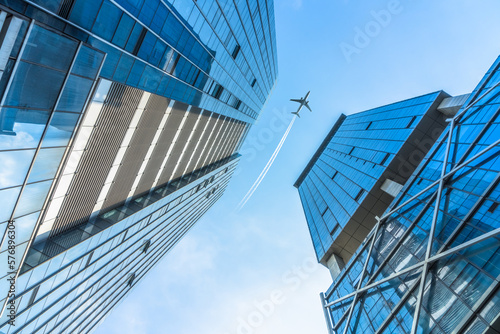 Tall city buildings and a plane flying overhead.