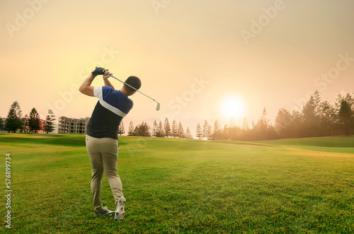 Man playing golf on a golf course in the sunrise. View from the back.