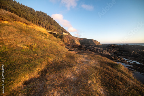 Rocky cliff and green grass at ocean beach at sunset time