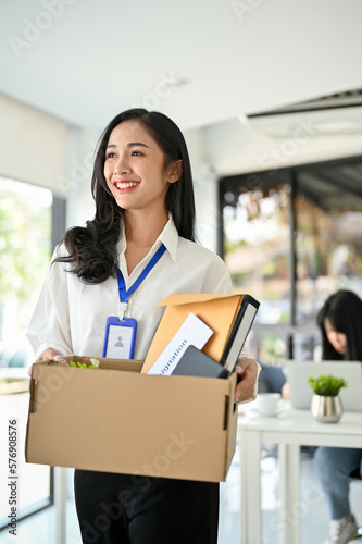 Beautiful Asian female office worker holding a cardboard box with her belongings, happy to resign.