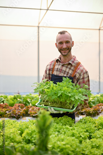 Smiling Caucasian male farmer holding a tray of vegetable seedlings