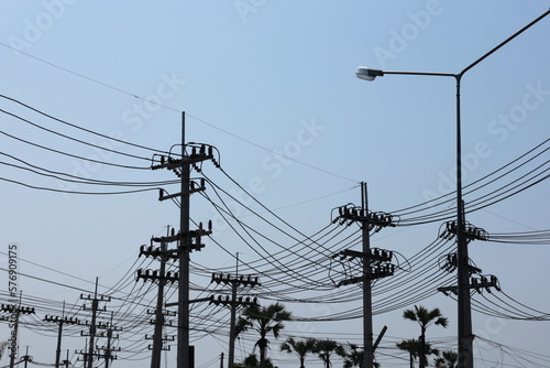 Silhouette of a strong electric line on a pole. Many high voltage transmission lines in front of a substation on the side of a highway in an urban area on a blue sky background. selective focus