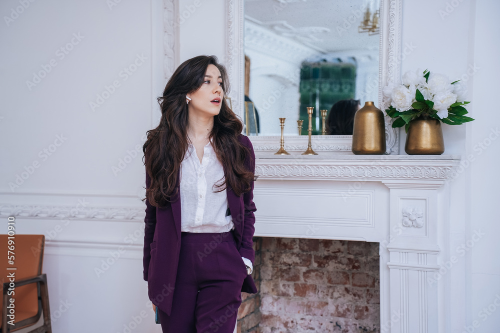 Exhausted Brunette Caucasian female entrepreneur in violet suit standing at home against classic interior with fireplace. Gorgeous Spanish businesswoman looks aside. Business people.