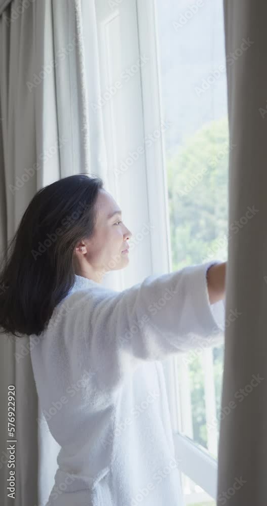 Vertical video of happy asian woman opening curtains in bedroom, in slow motion Vertical video of happy asian woman opening curtains in bedroom, in slow motion