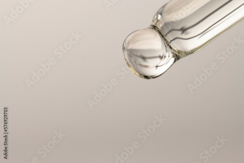 Macro of a glass dropper with essential oil for massage and spa on a gray background with copy space. Beauty procedures, body care.