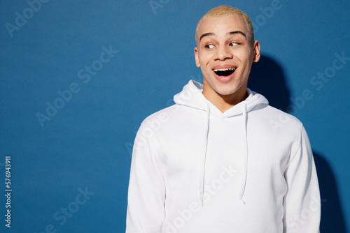 Stampa su tela Young astonished shocked amazed surprised impressed dyed blond man of African American ethnicity wear white hoody look aside on area isolated on plain dark royal navy blue background studio portrait