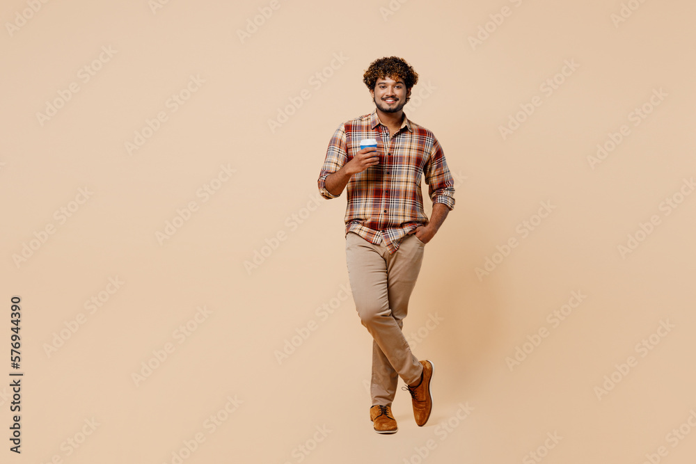Fototapeta premium Full body young Indian man wear brown shirt casual clothes hold takeaway delivery craft paper brown cup coffee to go isolated on plain pastel light beige background studio. People lifestyle concept.