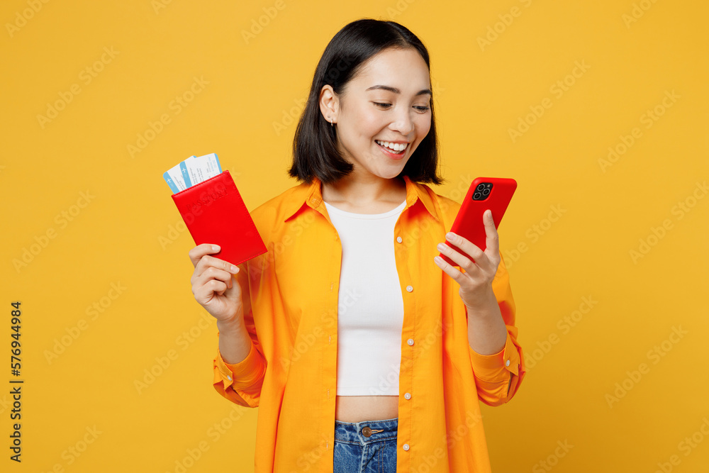Young woman wears summer clothes hold passport ticket use mobile cell phone isolated on plain yellow background. Tourist travel abroad in free spare time rest getaway. Air flight trip journey concept. Young woman wears summer clothes hold passport ticket use mobile cell phone isolated on plain yellow background. Tourist travel abroad in free spare time rest getaway. Air flight trip journey concept.