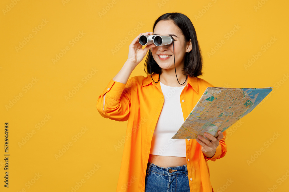 Young happy woman wear summer casual clothes hold in hand map use binoculars isolated on plain yellow background. Tourist travel abroad in free spare time rest getaway Air flight trip journey concept. - obrazy, fototapety, plakaty 