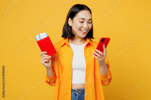 Young woman wears summer clothes hold passport ticket use mobile cell phone isolated on plain yellow background. Tourist travel abroad in free spare time rest getaway. Air flight trip journey concept. #576944984