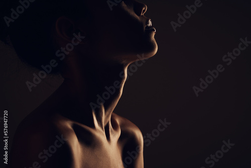 Beauty, woman and silhouette dark background of skin, body and model with glow, light and art on black. Face of aesthetic model person in studio for abstract, creativity and shadow profile or space