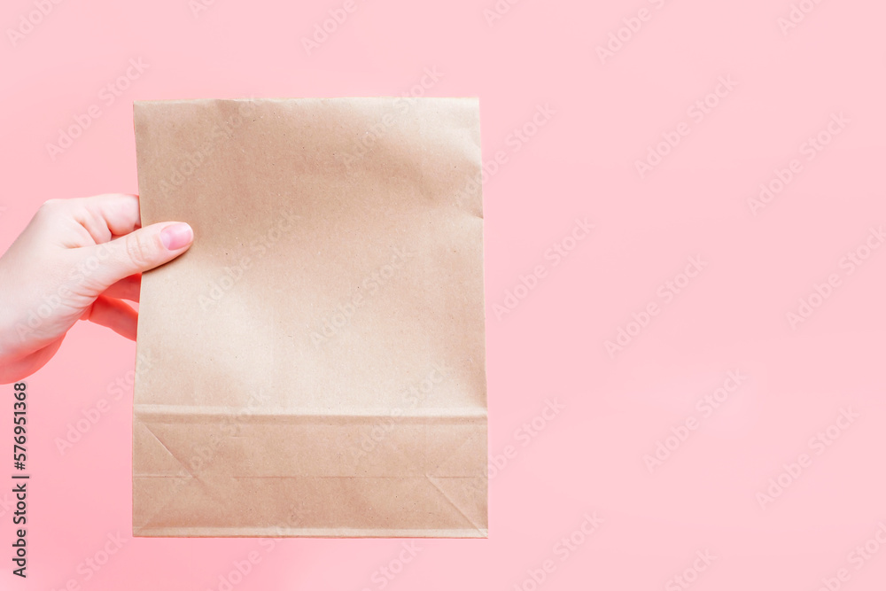 Female hand holding kraft paper bags on pink background, copy space. Female hand holding kraft paper bags on pink background, copy space.