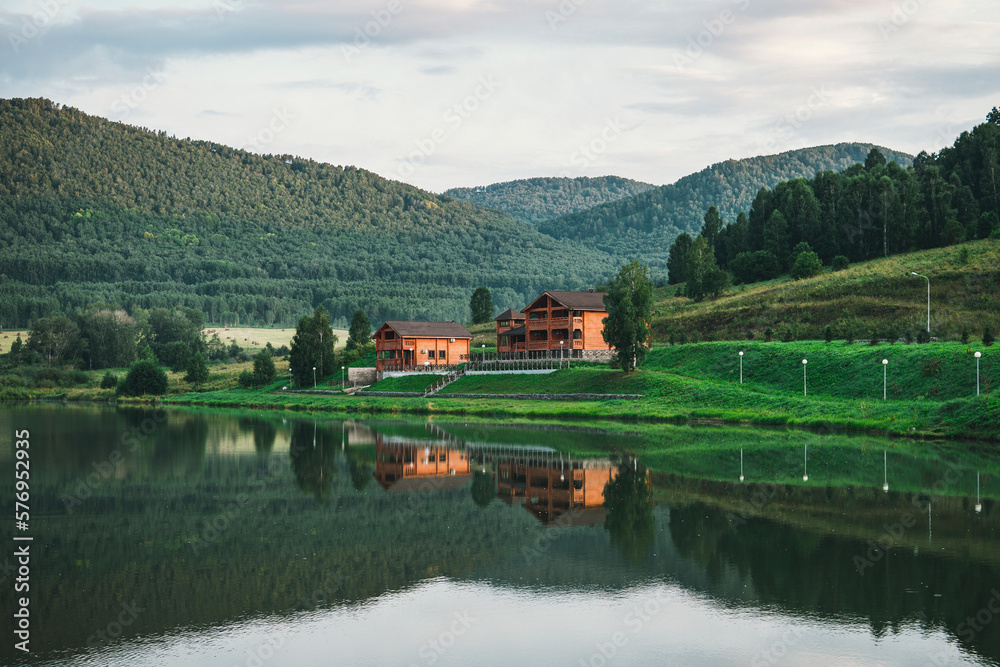 Log house outside the city for recreation. Ecologically clean region. Reflection of the house in the water of a clear lake. Beautiful landscape with cottage near a lake and trees. Log house outside the city for recreation. Ecologically clean region. Reflection of the house in the water of a clear lake. Beautiful landscape with cottage near a lake and trees.