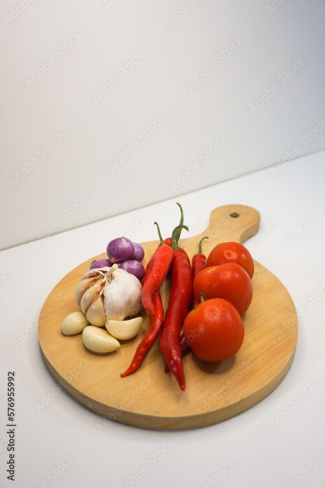Garlic, Chili, red onion and tomatoes on a wooden coaster, High Angle shot. Garlic, Chili, red onion and tomatoes on a wooden coaster, High Angle shot.